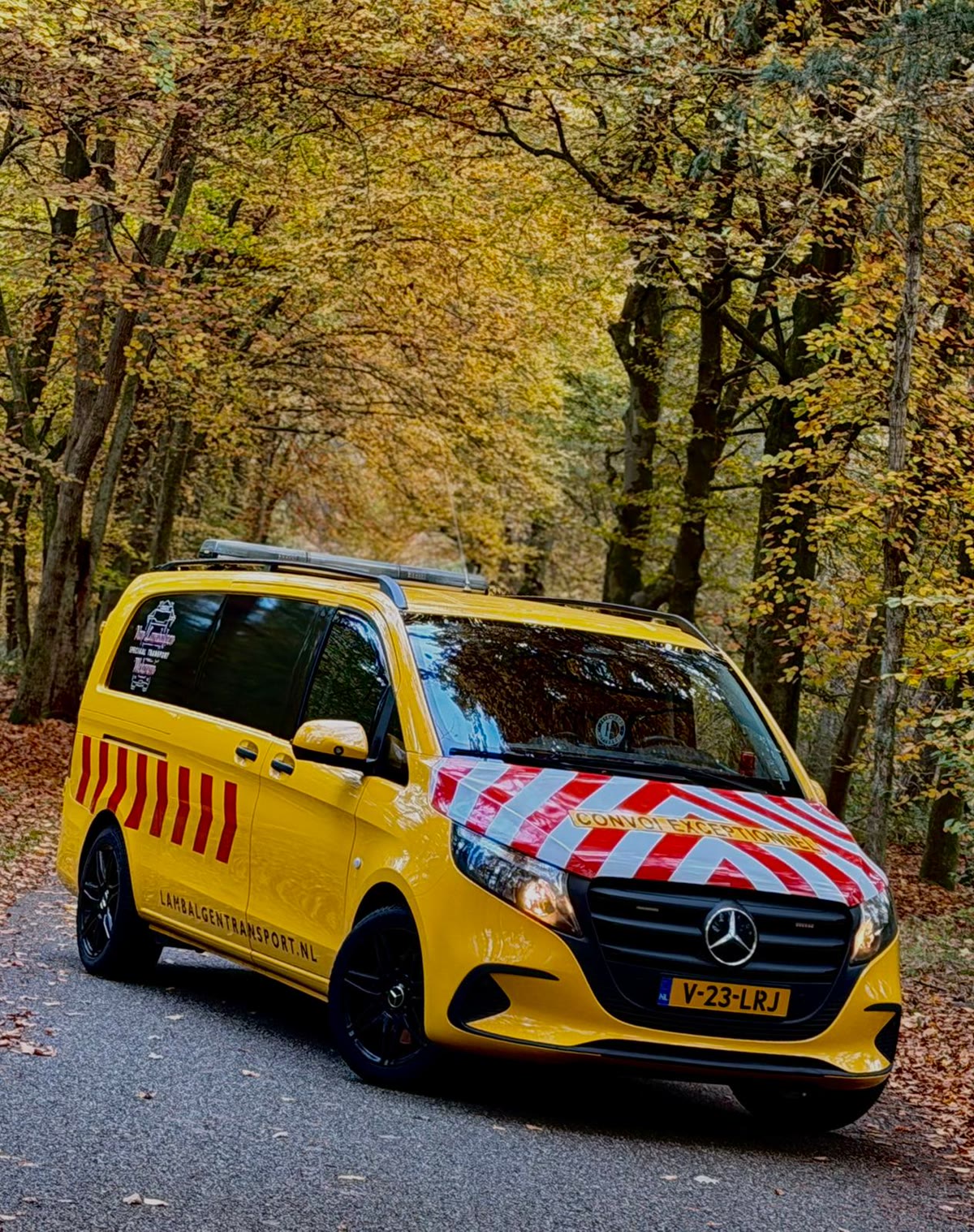 Geel begeleidingsvoertuig van Van Lambalgen in een herfstbos